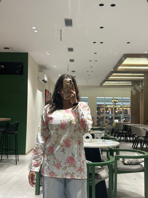 Person taking a mirror selfie in a modern cafe with floral top and jeans.